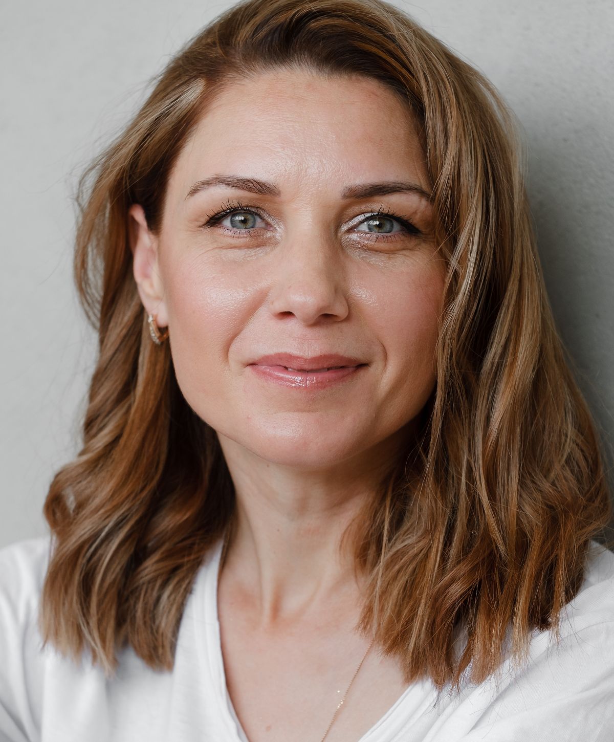 Smiling woman with wavy hair against a wall.