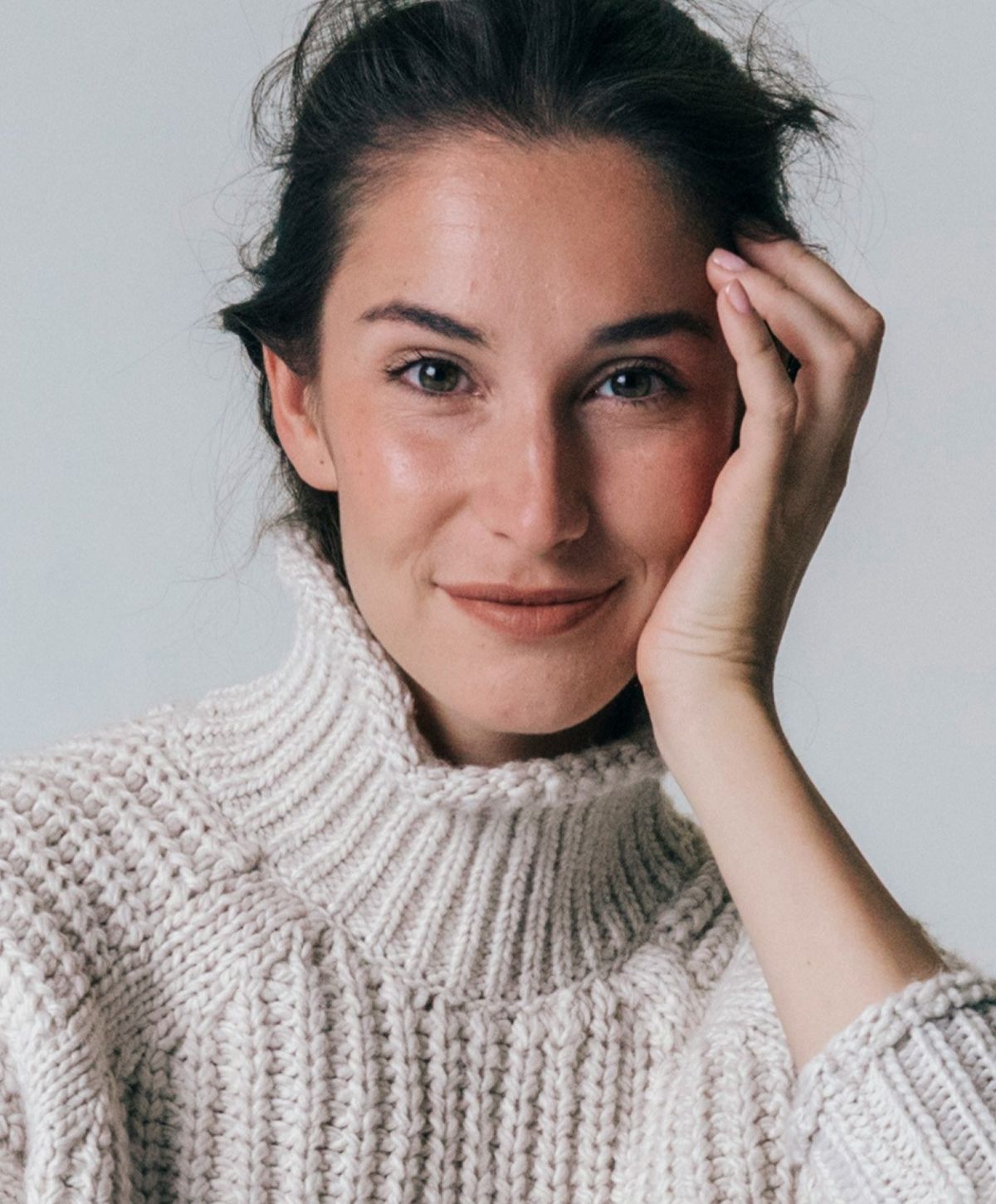 Smiling woman in cozy sweater, hand on face.