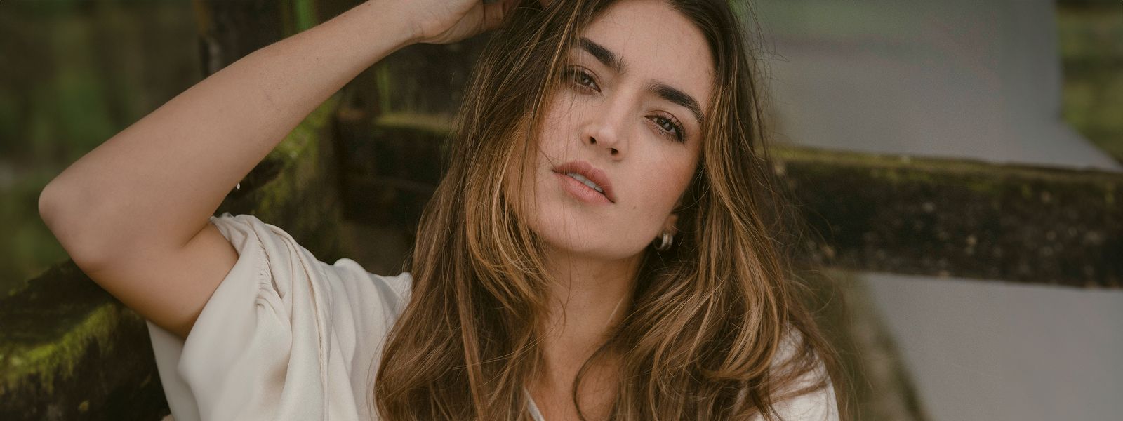 Woman with long hair posing thoughtfully outdoors.