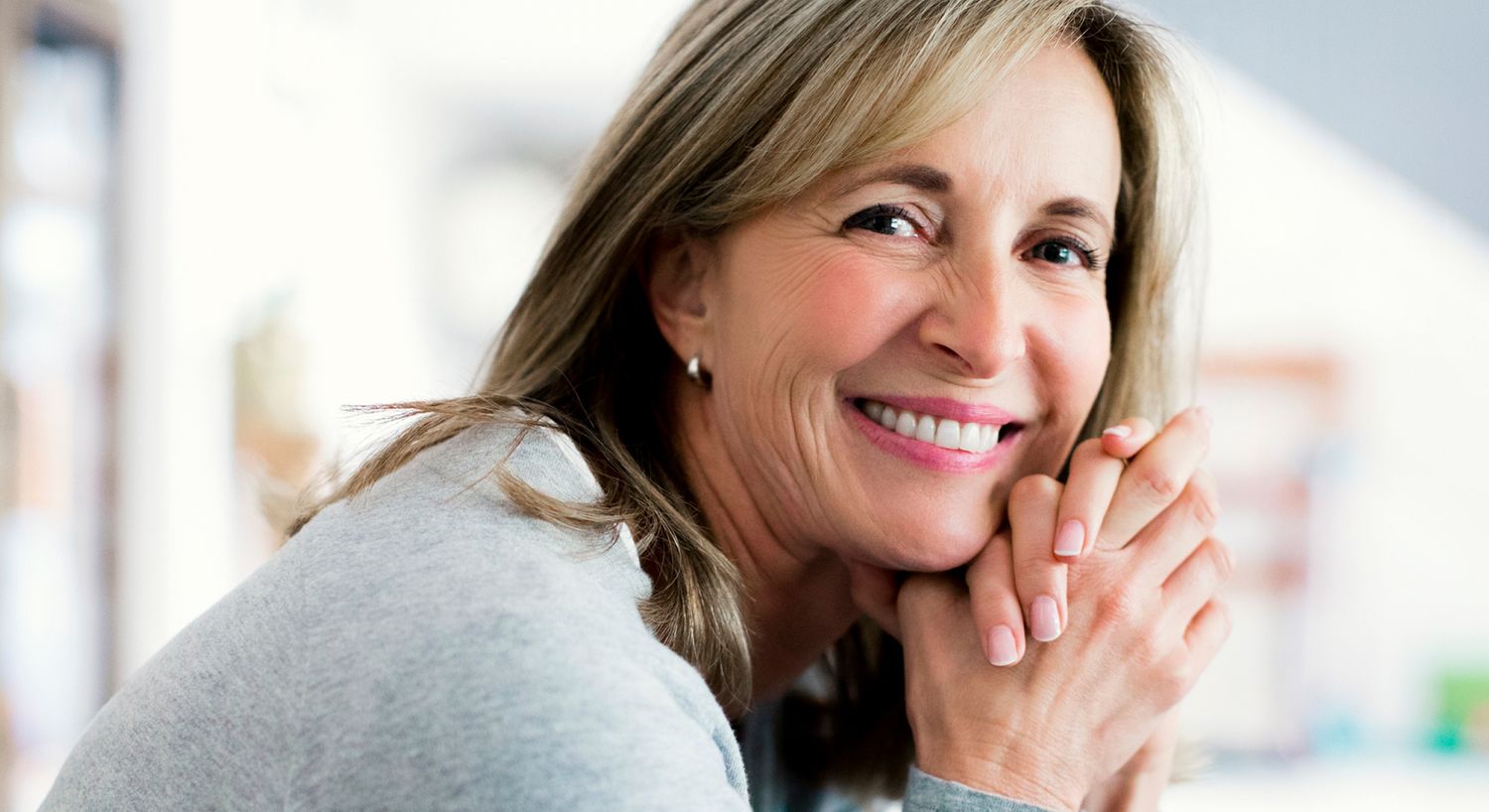 Smiling woman with long hair and hands clasped.